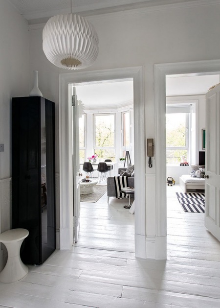 Biały pzredpokój z czarną szafą z widokiem na wnętrze mieszkania w stylu skandynawskim,