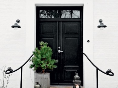 Białe ściany domu,czarne drzwi wejściowe,zielona choinka w szarym wazonie i metalowe latarenki na betonowych schodach (27412)