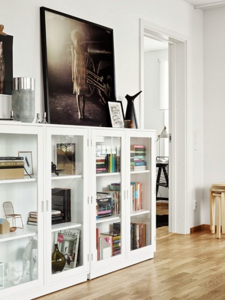 Niskie białe witryny,drewniany parkiet,czarne współczesne fotografie i grafiki w aranżacji skandynawskiego salonu