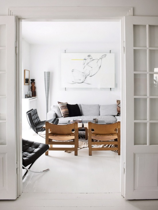 Nowoczesne grafiki,drewniane skandynawskie fotele,pikowany czarny fotel na metalowych nóżkach,szara sofa i biała podłoga w salonie