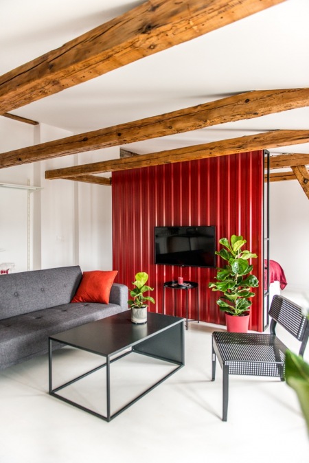 Oryginalna aranżacja salonu z drewnianymi belkami i czerwoną ścianą telewizyjną