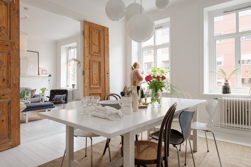 Postarzane dzrwi z białą patyną,biały stół prostokatny,różne krzesła w jadalni w stylu skandynawskim