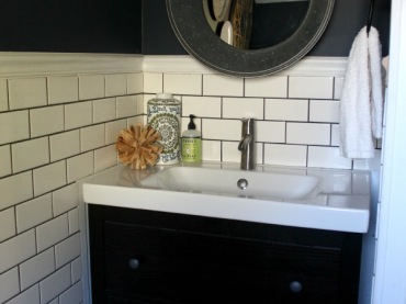 W małej łazienkowej wnęce umieszczono szafkę z umywalką. Mebel jest czarny, podobnie jak część ściany, co dodaje...