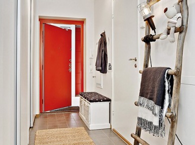 Biała szafka na buty,drewniana drabina z industrialną lampą w przedpokoju z czerwonymi drzwiami (24085)