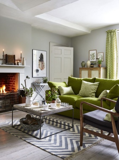 Zielona sofa i zielone dodatki w aranżacji salonu z kominkiem