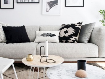 Szara sofa w salonie w stylu skandynawskim stanowi świetne tło dla czarnych poduszek ze wzorem i pozostałych dekoracji....