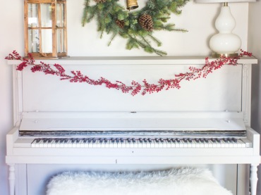 Białe pianino w salonie przystrojono drobnymi elementami. Girlanda z czerwonej jarzębiny pięknie się tu prezentuje. Zielony wianek oraz latarenka również nadają wnętrzu odświętny...