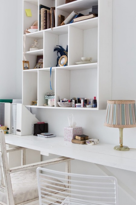 Biała wąska konsolka w roli domowego biurka przy ścianie z wiszącym prostym regałem z otwartymi pólkami