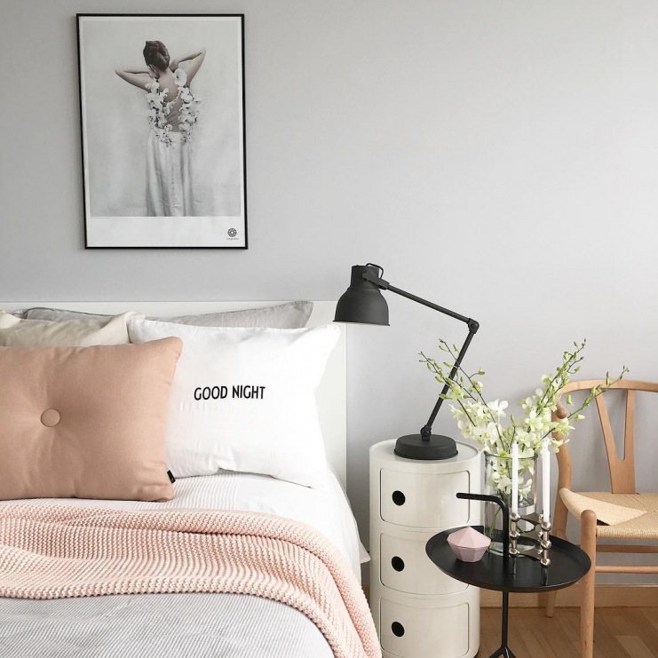 Szarość na ścianie w sypialni stanowi neutralne tło dla dodatków w innych odcieniach. Koc i poduszka w pastelowym różu...