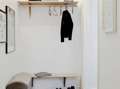 Drewniana podłoga i półki w małym przedpokoju,białe ściany,szara tapicerowana ławka,skandynawski biało-czarny dywanik (47831)