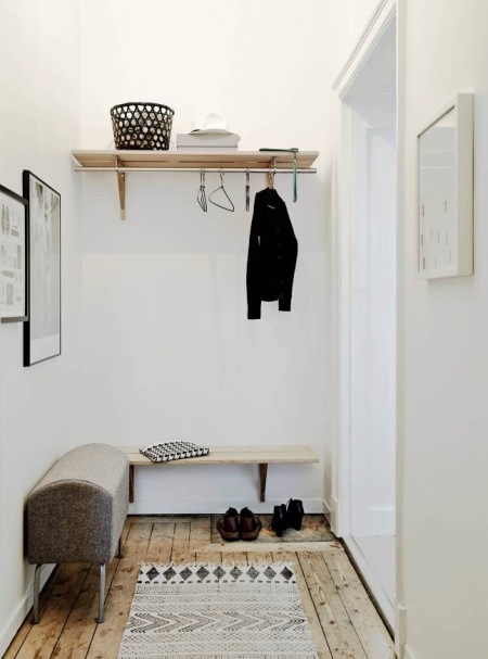 Drewniana podłoga i półki w małym przedpokoju,białe ściany,szara tapicerowana ławka,skandynawski biało-czarny dywanik
