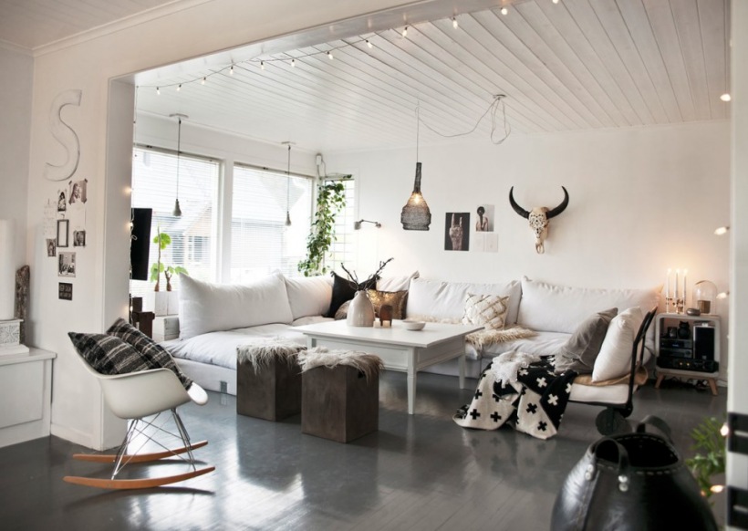 Biały otwarty salon z grafitową podłogą,girlandą z żarówkami, białymi sofami i fotelem na płozach