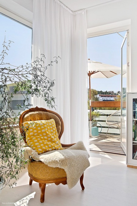 Stylowy fotel, białe zasłony  w salonie z balkonem