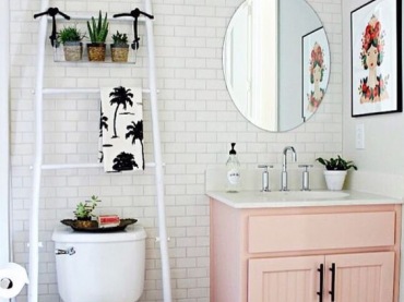 Wystrój łazienki urozmaica różowa szafka w pastelowym odcieniu. Na białej drabince można zawiesić ręczniki albo drobne...