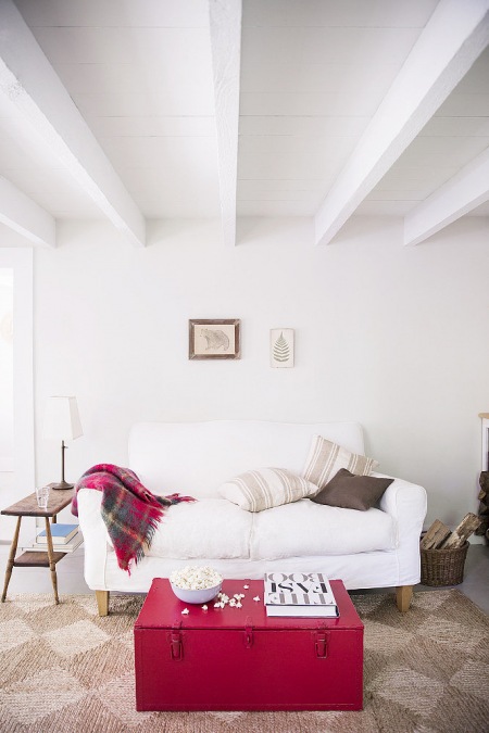 Różowy kufer skrzynia,drewniana ławka, jutowy dywan i biała sofa w rustykalnym salonie