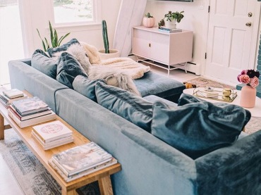 W aranżacji pokoju dziennego dominuje niebieski kolor. Ułożone na sofie duże poduszki z miękkiego materiału dodają...
