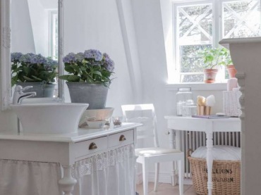 Salonowy klimat wnosi do łazienki ustawiony w oknie stoliczek z krzesłem oraz dywan. Ozdobny żyrandol i kwiaty w...