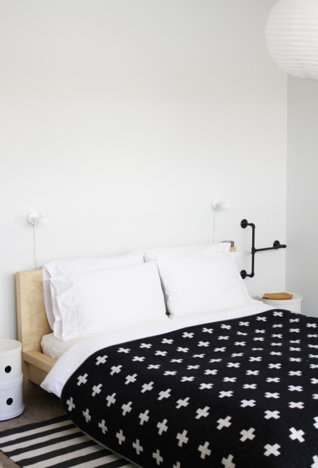 Drewniane łóżko,pasiasty dywan,czarna narzuta w białe gwiazdki
