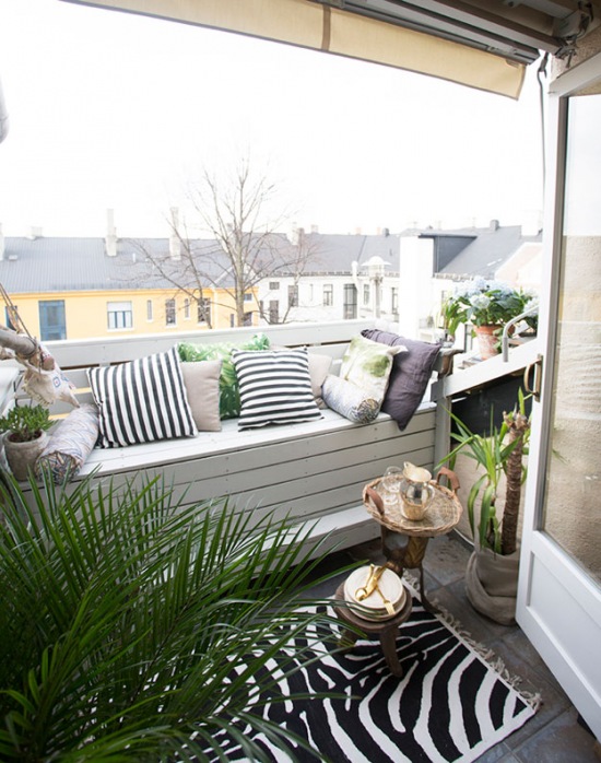 Aranżacja małego balkonu z drewnianą zabudową ze skrzynia i biało-czarnymi poduszkami