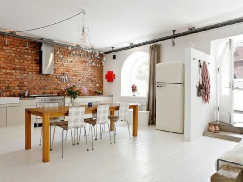 Druciane żyrandloe,biała podłoga,nowoczesne krzesła ,drewniany stół prostokatny i  ściana z czerwonej cegły w dużej otwartej kuchni