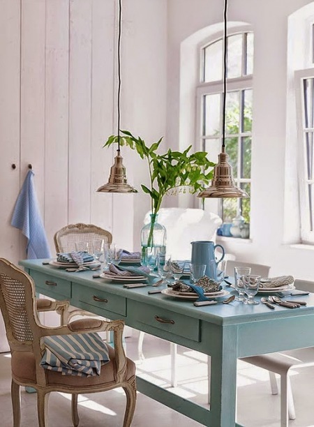 Niebieski drewniany stół jadalniany z szufladkami,miedzisne lampy wiszące i rattanowe krzesło w jadalni