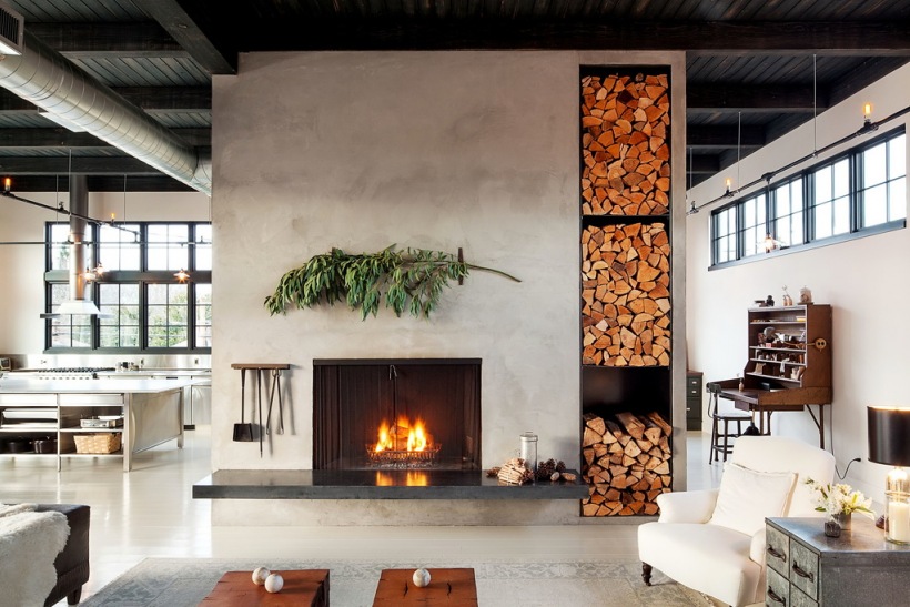 Betonowa ściana z kominkiem i wnękami na składowanie drewnia kominkowego w otwartej przestrzeni salonu w stylu industrialnym