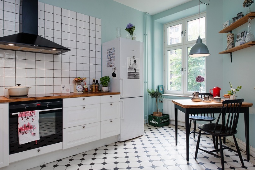 Czarny okap, białe szafki kuchenne z drewnianym blatem,turkusowo-mietowe ściany,biało-czarna terakota na podłodze w kuchni z czarnym stołem i krzesłami