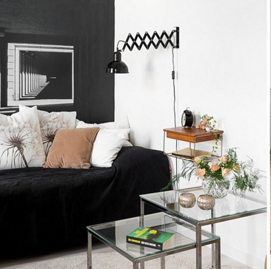 Czarna ściana z perspektywą,czarny kinkiet  z wysięgnikiem na białejścianie w salonie,czarna sofa,biale i brązowe poduszki,chromoniklowane stoliki ze szklanym blatem