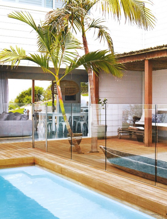 Szklana balustrada wokół basenu,drewniane deski na tarasie z rustykalnym dachem pośród egzotycznych palm