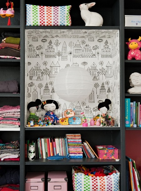 Czarny regał z otwartymi półkami w fantazyjną tapetą wenątrz wnęki i kolorowymi dekoacjami i produktami dla dziecka