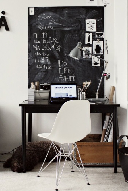 Czarne  małe biurko,czarna tablica z farba tablicową,białe nowoczesne krzesło na metalowych krzyżakach,drewniana skrzynka i szara metalowa lampa na biuo w domowym miejscu do pracy