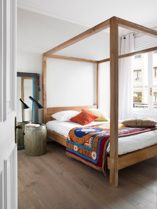 Kolorowa narzuta w etniczne wzory na łóżku z drewnianą konstrukcją wysokich ram