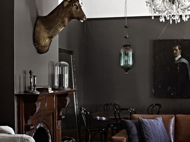 Eklektyczny salon z czarnymi ścianami,stylowym brązowym kominkiem,kryształowym żyrandolem i lampionem z zielonym szkłem (21525)