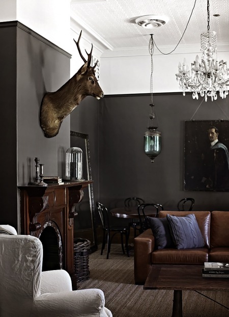 Eklektyczny salon z czarnymi ścianami,stylowym brązowym kominkiem,kryształowym żyrandolem i lampionem z zielonym szkłem