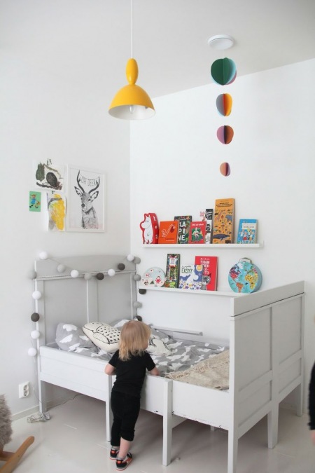 Girlanda z bawełnianych kul,wąskie półeczki na ścianie i drewniane łóżko dla przedszkolaka