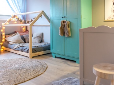 W pokoju dziecięcym znajduje się charakterystyczne łóżko w kształcie domku oraz niebieska szafa do przechowywania...