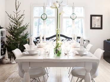 Typowo skandynawska dekoracja świątecznej jadalni, w której dominuje biel oraz zielone naturalne akcenty. Skromna zastawa na stole i choinka w swojej surowej postaci przełamują jasną kolorystykę wnętrza i wnoszą do niego delikatny gwiazdkowy...