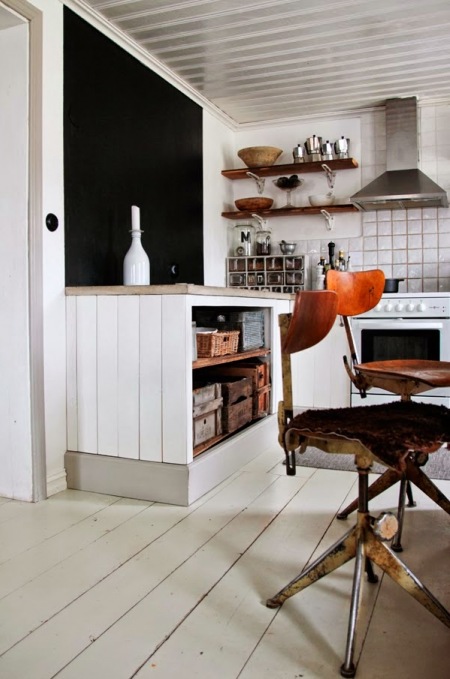 Otwarte białe szafki kuchenne  z drewnianymi blatami w stylu vintage,czarna ściana, drewniane półki i industrialne krzesła vintage