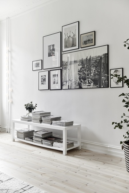 Biała niska konsolka z pólkami w salonie z białymi ścianami,galeria nowoczesnych fotografii w czarnych wąskich ramkach na ścianie