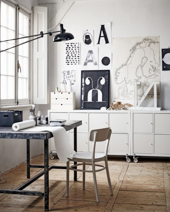 Białe komody na kółkach,czarno-białe grafiki w stylu skandynawskim,metalowe biurko i czarna lampa z wysięgnikiem w domowym biurze