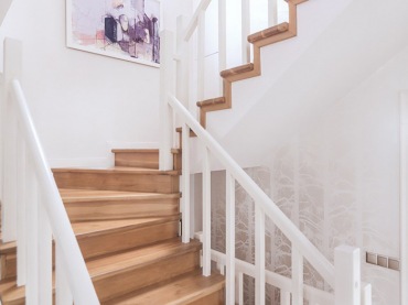 Drewniane schody w białym kolorze rozświetlają przestrzeń. Klatkę schodową znacząco dekoruje abstrakcyjny obraz, który...