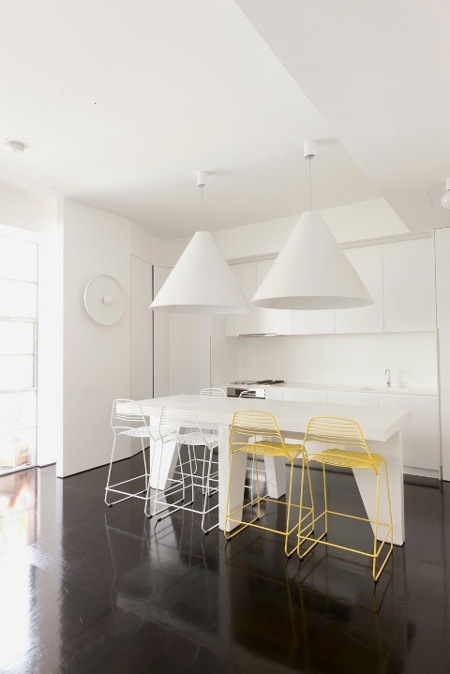 Dizajnerska minimalistyczna kuchnia w bieli z czarną zywiczna podłogą i biało-żółtymi ażurowymi krzesłami