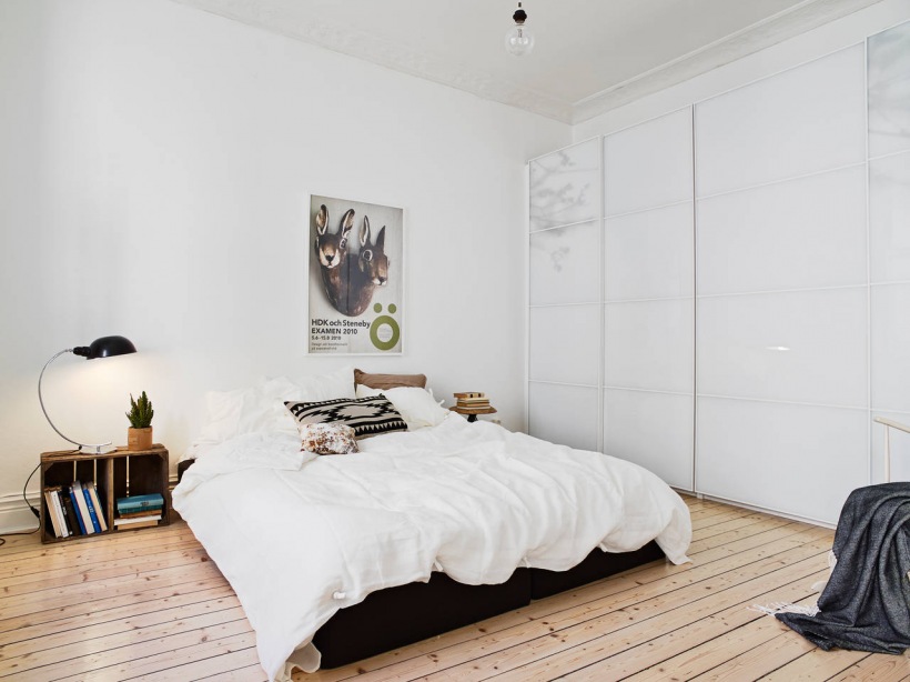 Nowoczesna szafa ze szklanymi drzwiamim przesuwnymi,podłoga z naturalnych desek i drewniane skrzynki w białej sypialni