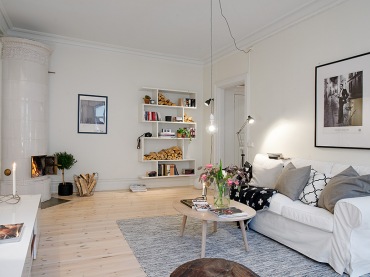 Skandynawski styl w pokoju dziennym - jasna drewniana podłoga, żarówka na kablu w minimalistycznym stylu, biała sofa...