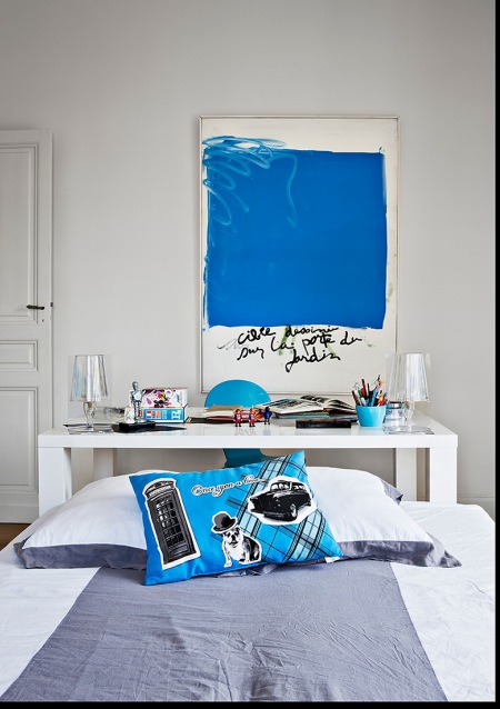 Nowoczesny obraz z niebieskim motywem,niebieska poduszka i detale w białej sypialni z biurkiem
