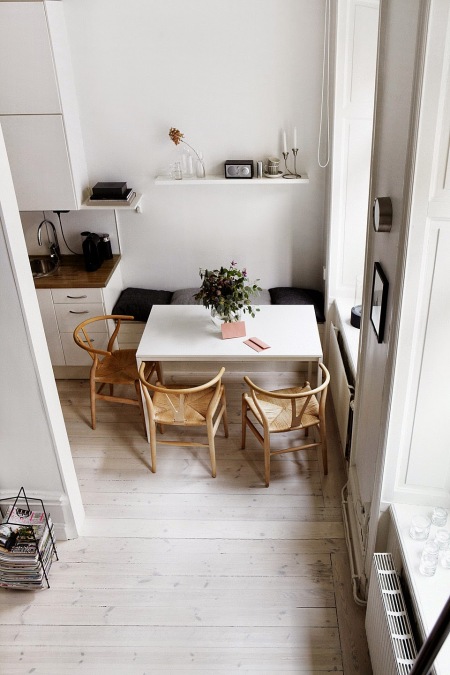Biały nowoczesny stół w jadalni przy kuchni z zabudowanymi siedziskami i drewnianymi skandynawskimi krzesłami z plecioną jutą