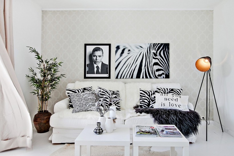 Czarno-białe fotografie postaci i zebry,gaficzne poduszki,czarna lampa na trójnogu,glinaiany wazon i biala sofa w salonie