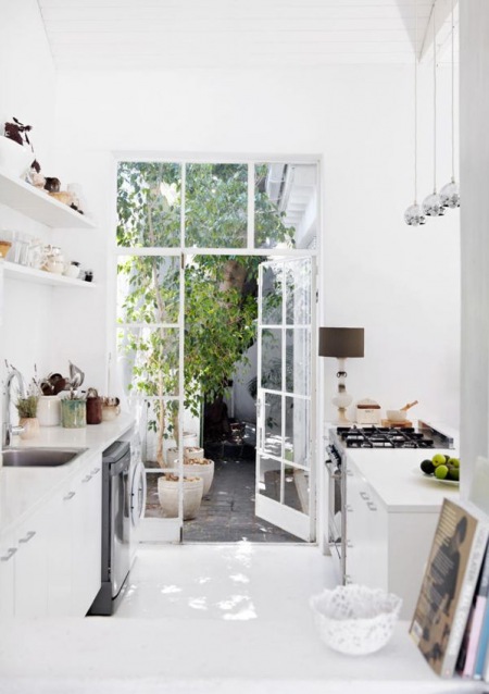 Aranżacja białej wąskiej kuchni z przeszkloną ścianą z drzwiami