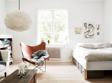 Lampa pompon,drewniana skrzynia,fotel skórzany motyl i łóżko w salonie małego mieszkania (24694)