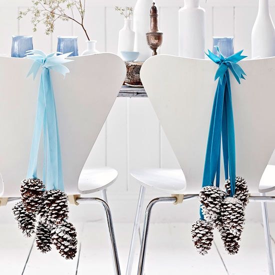 Pomyslowa dekoracja białych krzeseł szyszkami na niebieskich wstążkach